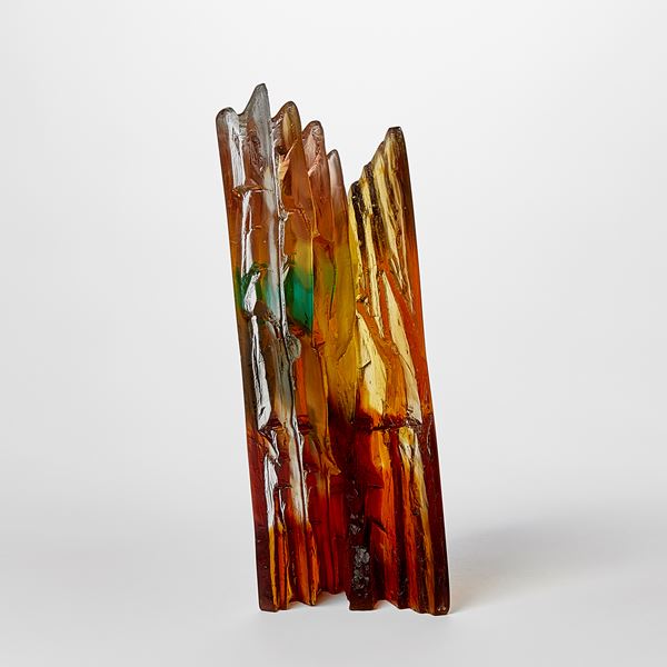 angular free standing amber rust green and yellow transparent sculpture with two flat polished surfaces and two inner ones with rugged and textured detail hand made from cast glass 