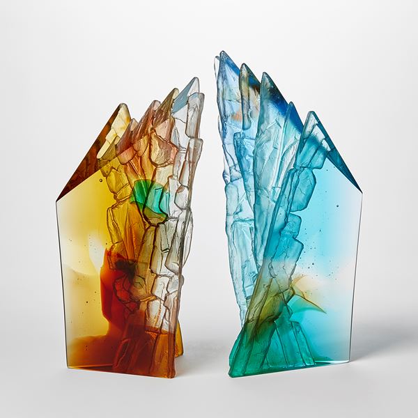 angular free standing amber rust green and yellow transparent sculpture with two flat polished surfaces and two inner ones with rugged and textured detail hand made from cast glass 