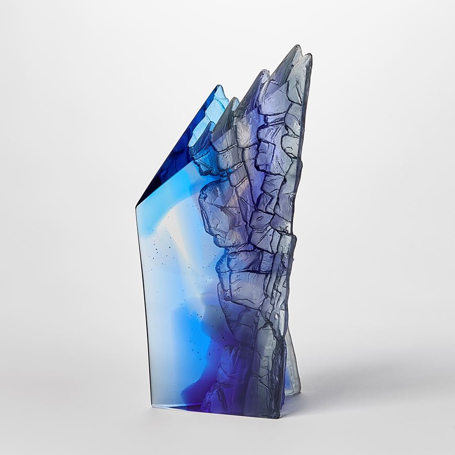 mixed blues cast glass sculpture inspired by rocky cliff edges with angular form and two polished sides with two additional sides covered with intense rough detail