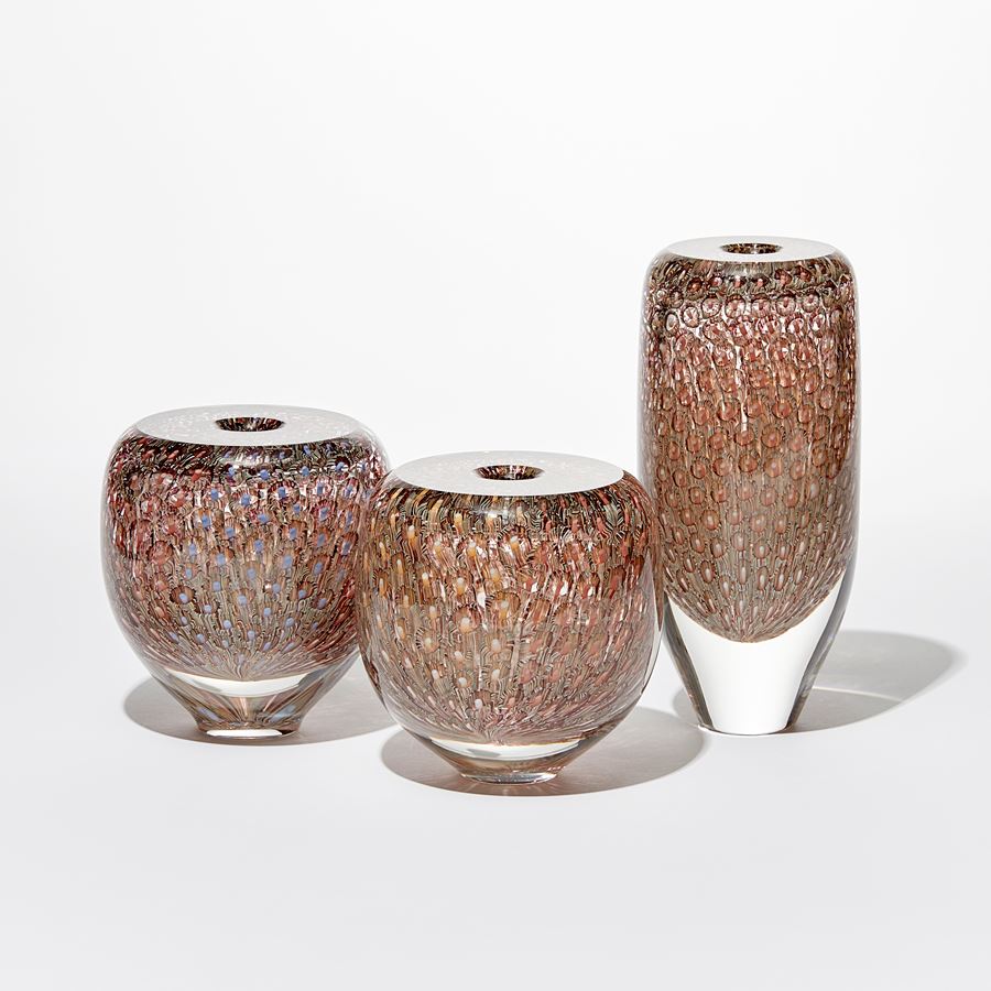 transparent tall round vessel with flat top and small aperture opening with fine repeat surface pattern in aubergine salmon and warm yellow hand made from glass