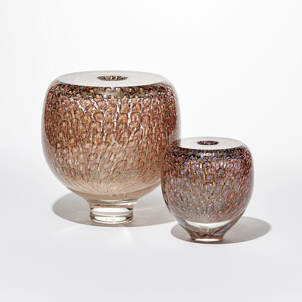 shiny transparent heavy round vessel with flat top and small central opening covered in an embedded fine repeat organic pattern in coral salmon aubergine and soft yellow hand made from glass