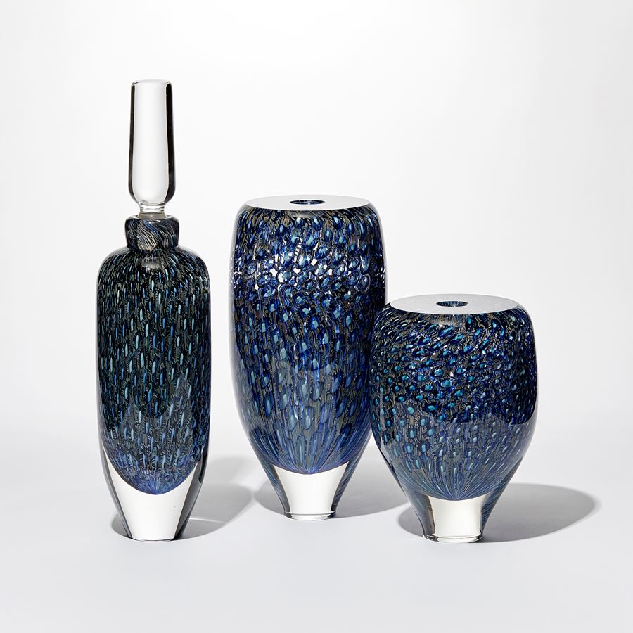 tall rounded transparent bottle with long elegant clear stopper with the main body covered in an fine intense organic repeat pattern in blue indigo turquoise jade and aquamarine hand made from glass 