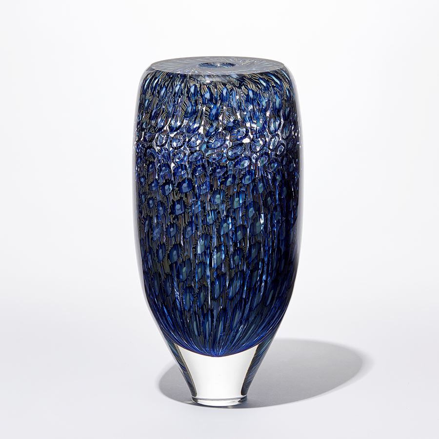 transparent rounded tall tapering at the base vessel with flat top and small central opening covered in a fine detailed intense pattern in blue indigo turquoise and aquamarine handmade from glass