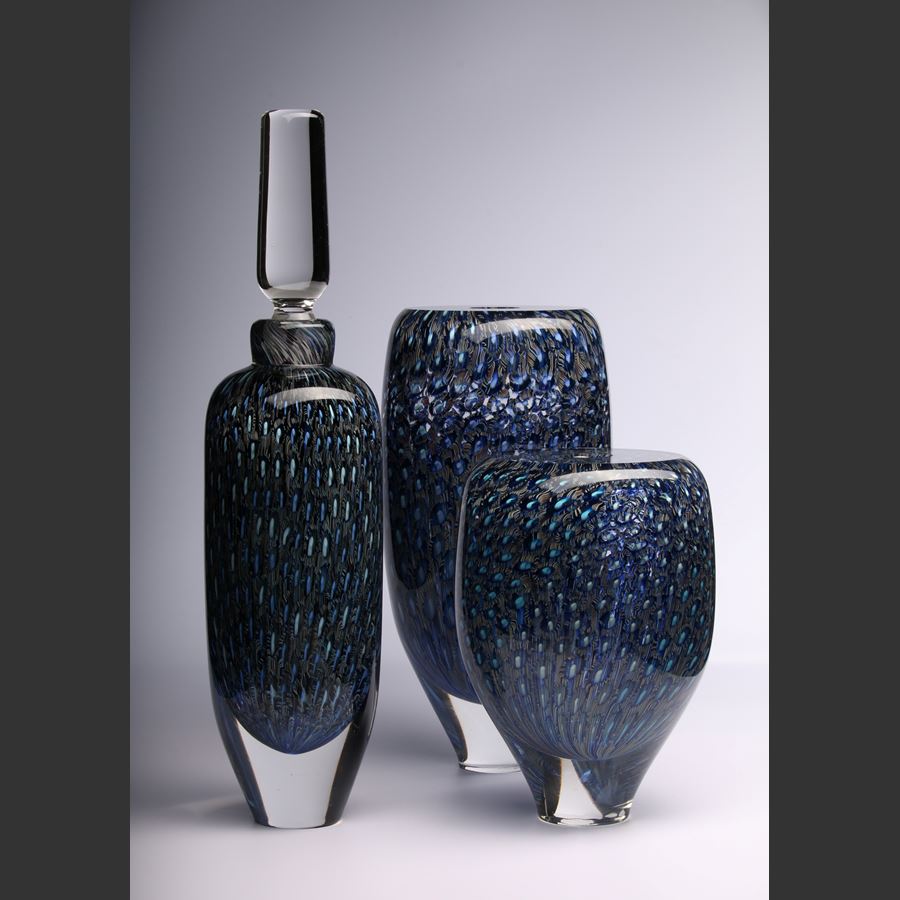 tall rounded transparent bottle with long elegant clear stopper with the main body covered in an fine intense organic repeat pattern in blue indigo turquoise jade and aquamarine hand made from glass 