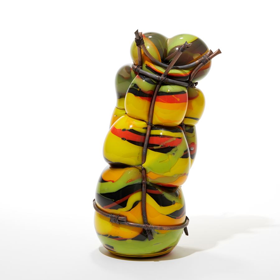 hand made  and blown lime green orange red and black organically banded standing  glass sculpture held within a copper cage and bulging between the gaps