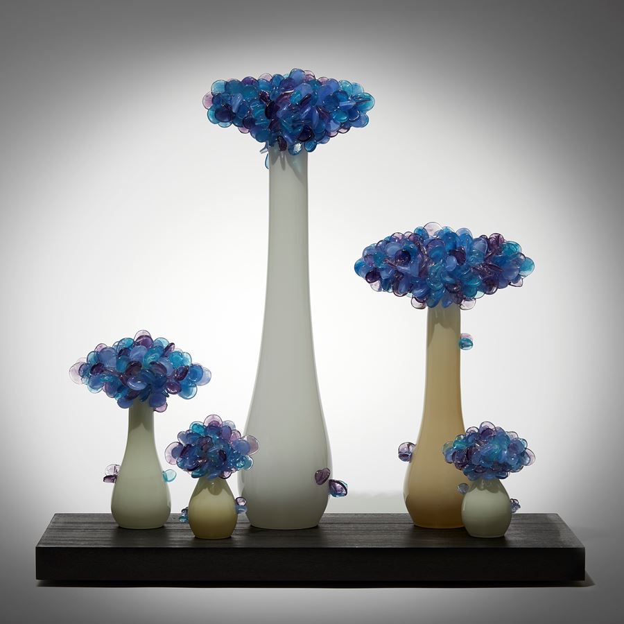 rectangular black wooden base with bonsai inspired trees set on its top each with bulbous rounded bases and clusters of lollipop shaped various blue and purple leaves hand made from glass