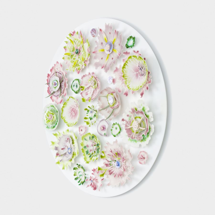 flat white round vertical opaque disc covered in organic abstract finely detailed floral and coral reef inspired relief adornments in pink aubergine lime green and dark apple green hand made from glass