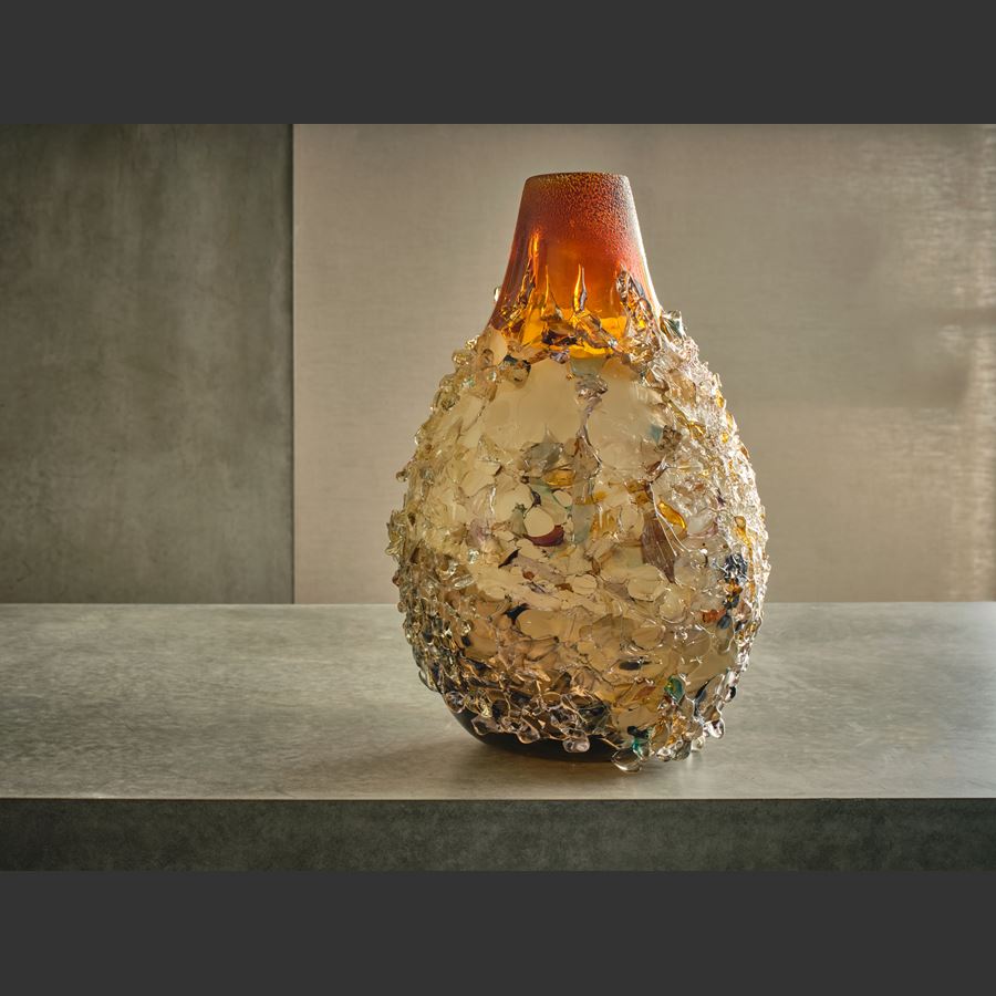 teardrop shaped vase covered in multicoloured shards with an opaque caramel base with a rich amber red top section hand made from glass
