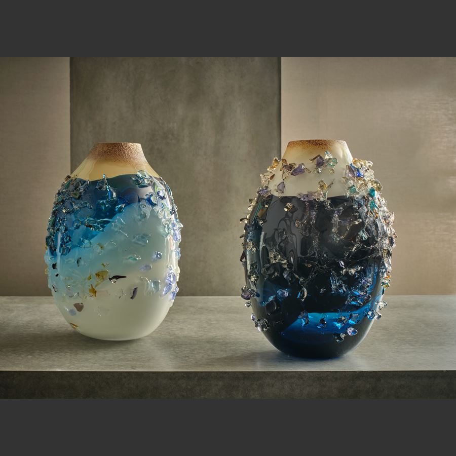 oval vase with milky white base fading to a turquoise banded middle with transparent blue upper topped with an opaque Cappuccino coloured top with the entire surface covered in multicoloured shards hand made from glass