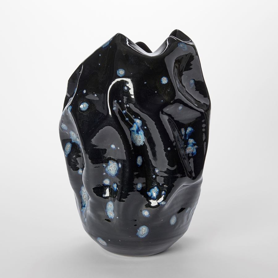 crumpled wrinkled and undulating vessel with glossy black surface with blue ink blot irregular details hand made from ceramics