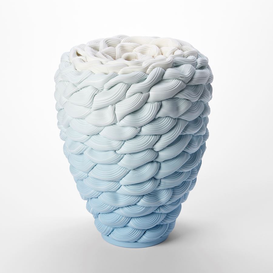 inverted teardrop standing vessel with small top opening and with the appearance as if made from stacked soft loops of ridged clay with a blue base fading to the top which is white hand made from parian porcelain