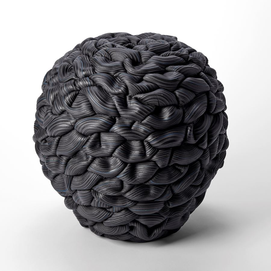 black and blue round vessel with the appearance as if made from interwoven and stacked ridged thick black rubber bands each creating soft folds and layers hand made from porcelain and parian 