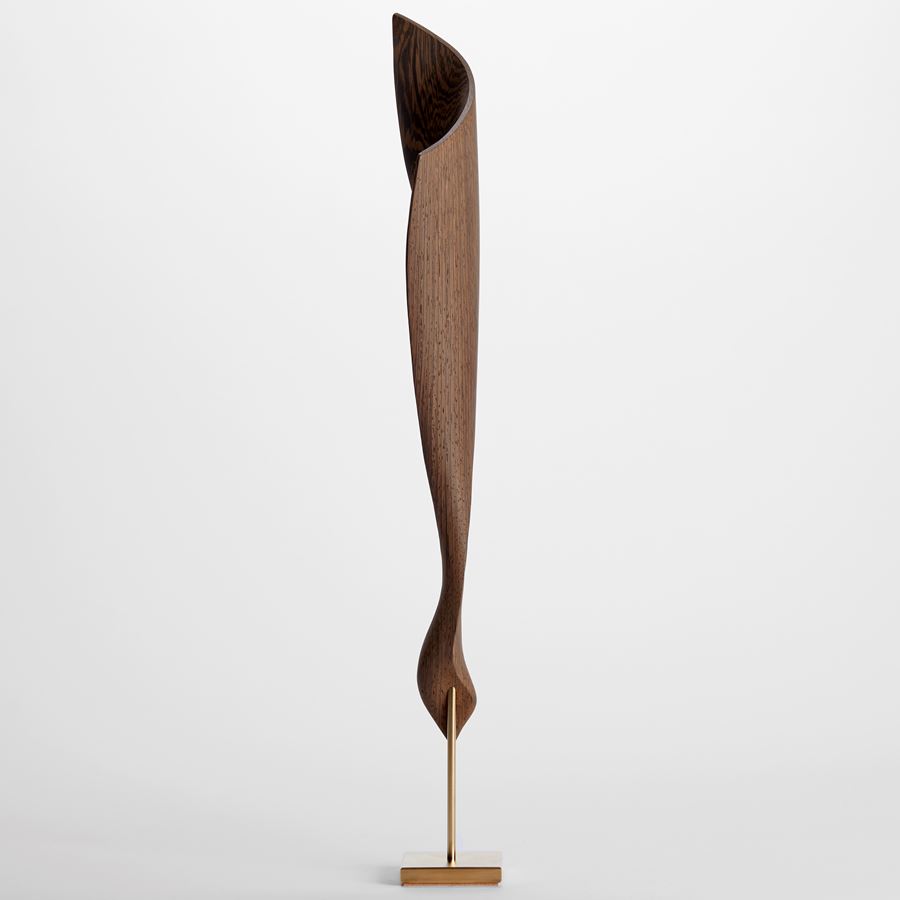 abstract curved highly grained wenge wood sculpture with lower curled section and upper wider sail form with fine gold inlaid detail and held aloft on a gold plated stand
