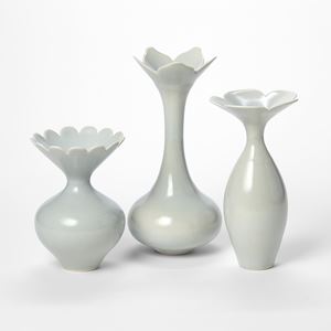 a trio of three elegant porcelain vases with narrow necks and each with open wide rims with petal shaped edges each in a soft dove grey blue colour hand made and thrown from porcelain