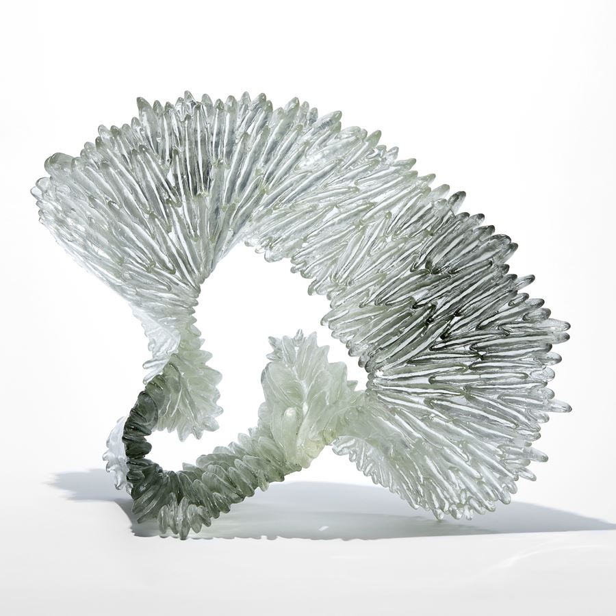 clear and grey looped organic standing sculpture with front face covered in rocky thin shards sitting proud from the surface like the gills on a mushroom hand made from cast glass