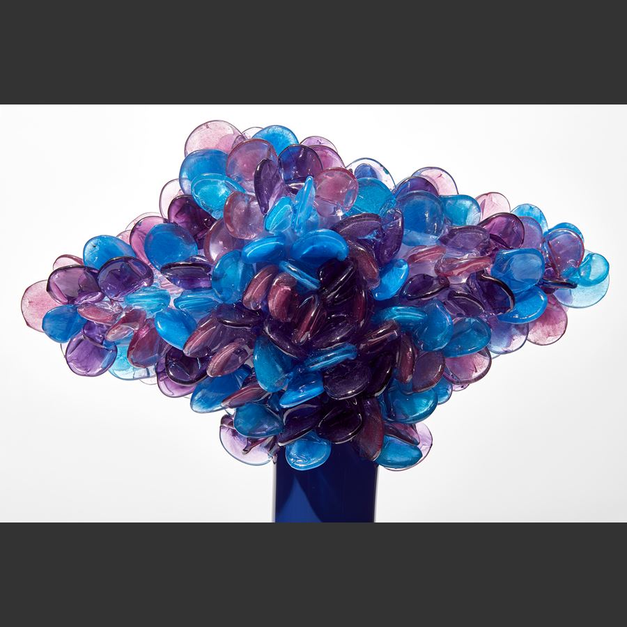 tall tree sculpture with long elegant thin trunk in opaque royal blue with diamond shaped canopy covered in lollipop shaped leaves in blue purple and lilac hand made from glass