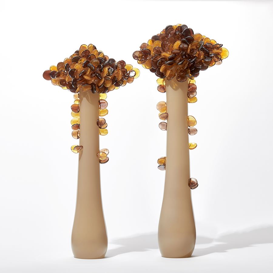 tall abstract tree sculpture with long opaque bronze trunk with diamond shaped canopy covered in lollipop shaped leaves in amber and brown handmade from glass