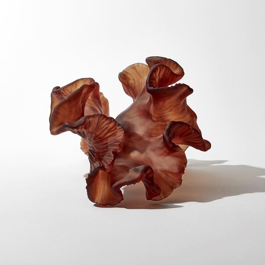 rich dark burnt orange amber organic arched frilled sculpture with the appearance of sea adrift seaweed with one smooth side and one slightly ridged hand made from glass