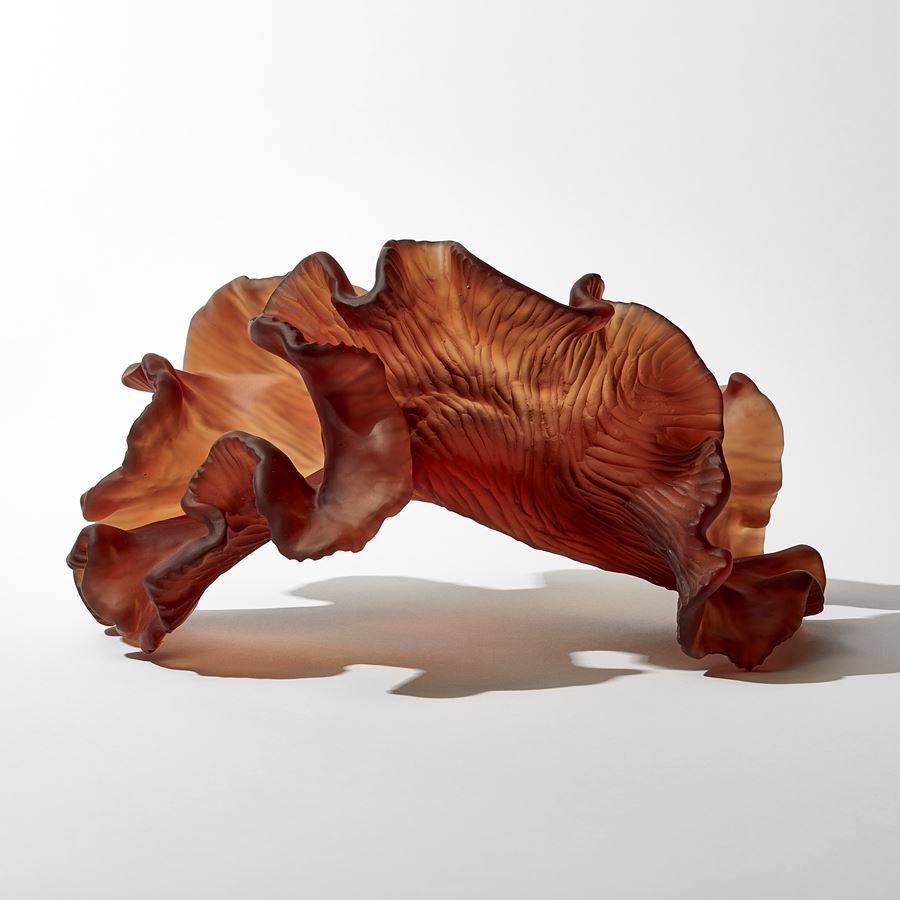 rich dark burnt orange amber organic arched frilled sculpture with the appearance of sea adrift seaweed with one smooth side and one slightly ridged hand made from glass