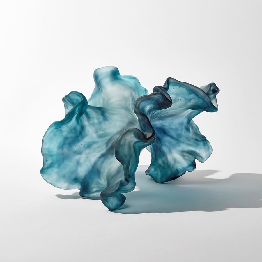 abstract swirling clear and jade blue sculpture with the appearance of a piece seaweed floating under water with frilled edges hand made from cast glass