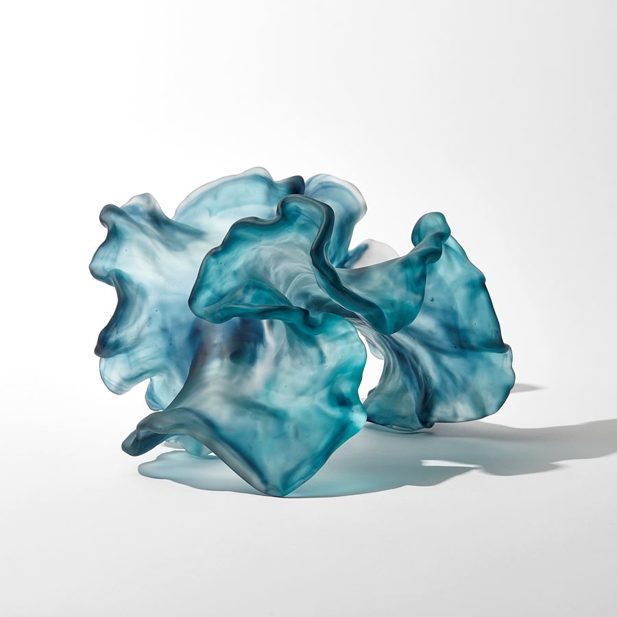 abstract swirling clear and jade blue sculpture with the appearance of a piece seaweed floating under water with frilled edges hand made from cast glass