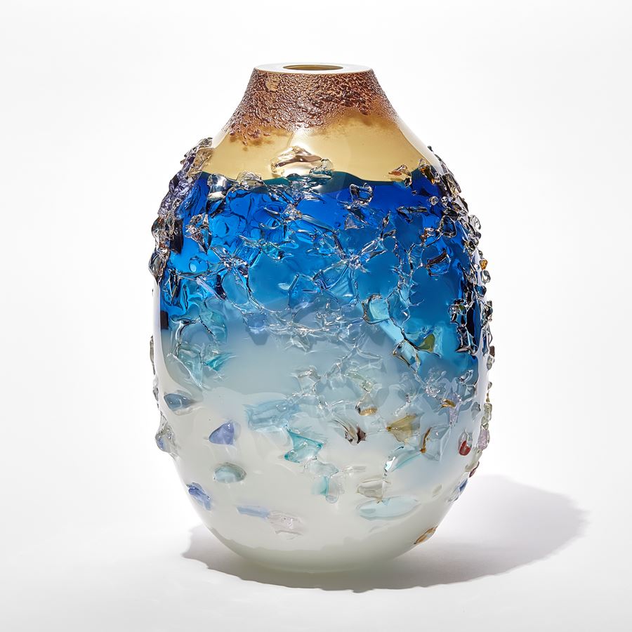 oval vase with milky white base fading to a turquoise banded middle with transparent blue upper topped with an opaque Cappuccino coloured top with the entire surface covered in multicoloured shards hand made from glass