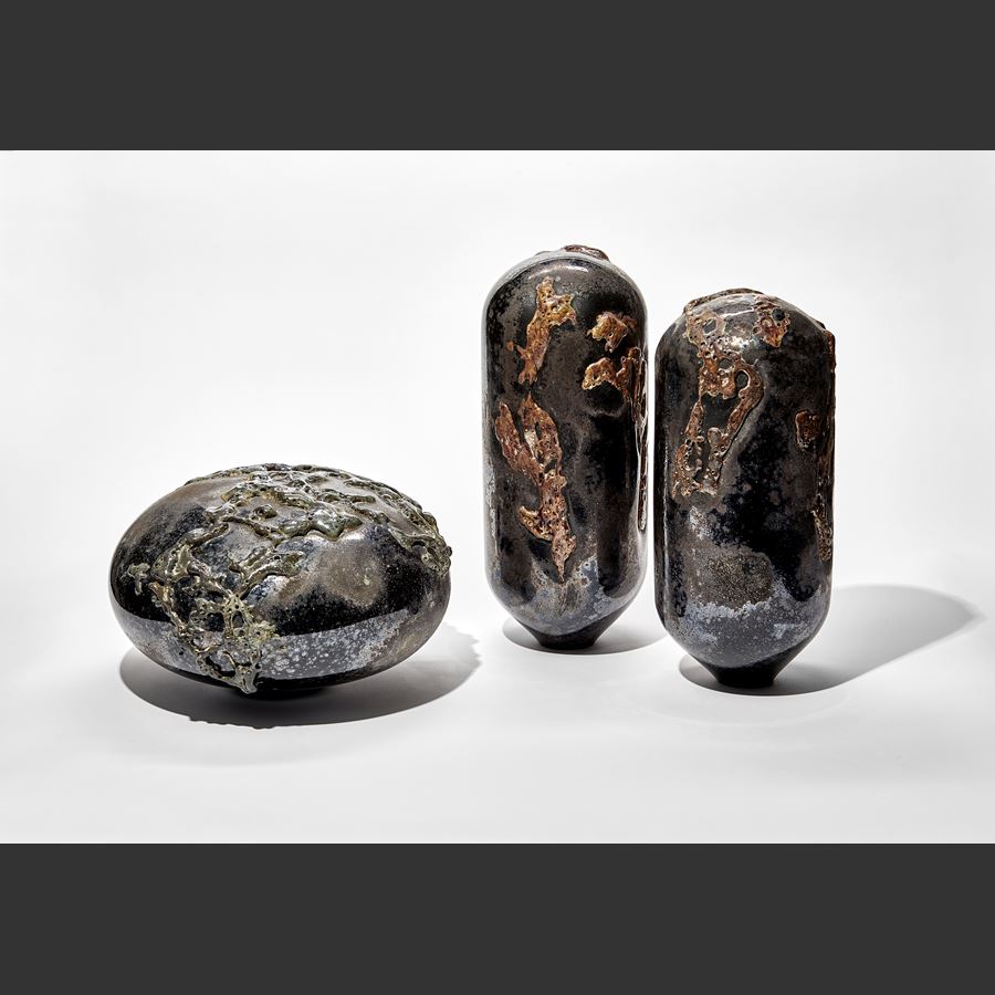 black rounded low mushroom shaped sculpture with leathery weathered surface covered in organic raised surface texture with a dark metallic sheen hand made from glass