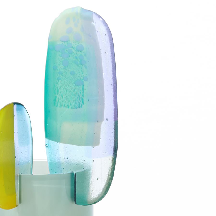 short opaque celadon cylinder with three rounded petals overlapping and perched on the top rim in lilac jade lime green and clear hand made from blown and fused glass