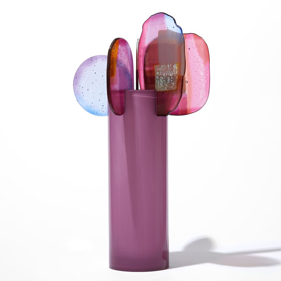 opaque raspberry pink cylinder with five rounded finals with abstract patterns in pink blue purple and gold perched on the top edge hand made from blown and fused glass