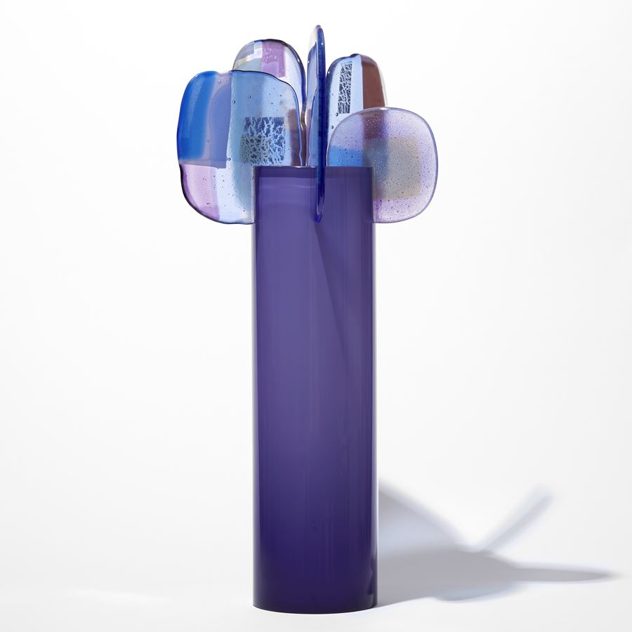 opaque purple cylinder with five simplified petals perched with abstract patterns on the top rim in blue lilac grey and brown hand made from glass
