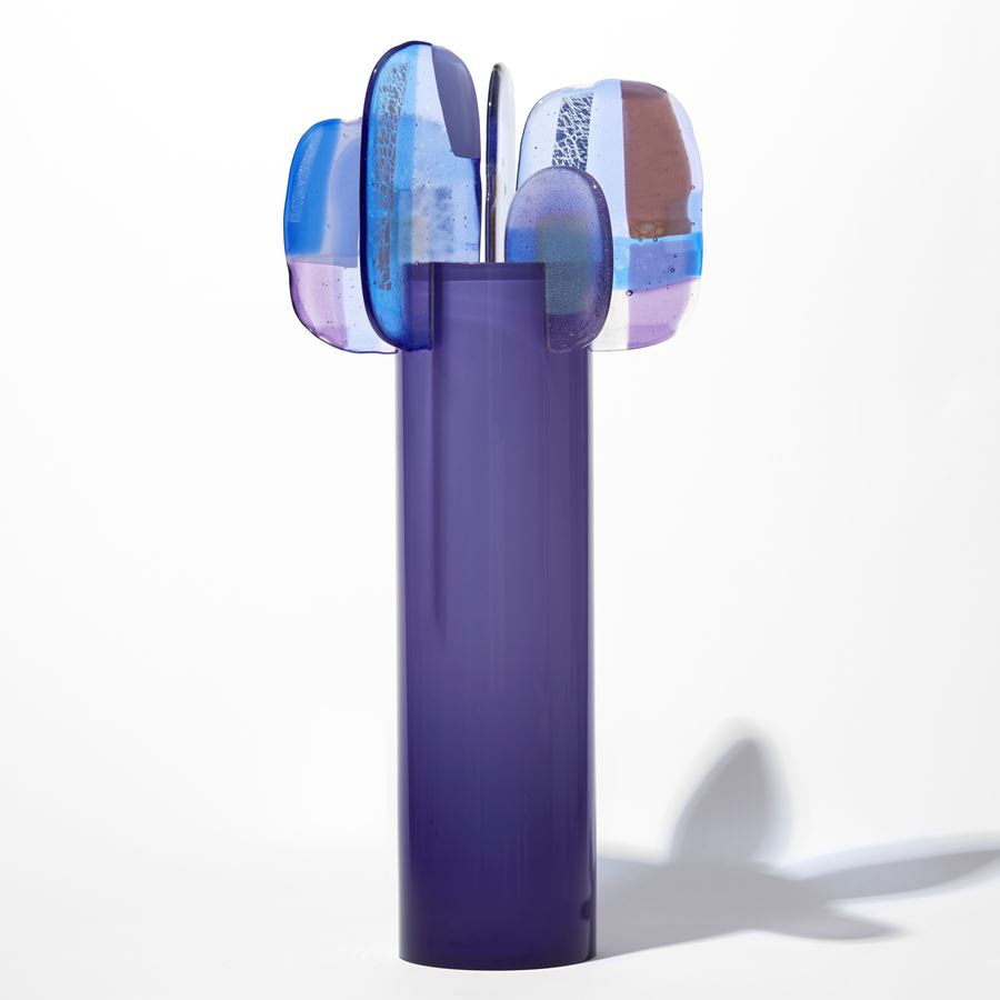 opaque purple cylinder with five simplified petals perched with abstract patterns on the top rim in blue lilac grey and brown hand made from glass