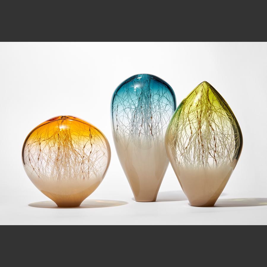 round transparent abstract glass sculpture with soft opaque fading light bronze base and golden yellow top  with clear middle trapped inside are a multitude of criss crossing thin white canes some with bulbous sections that are gold