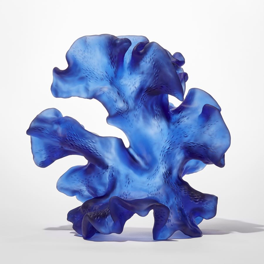 standing opaque blue frilled and undulating sculpture with the appearance of a piece of sea drift floating seaweed full of movement and made from cast glass