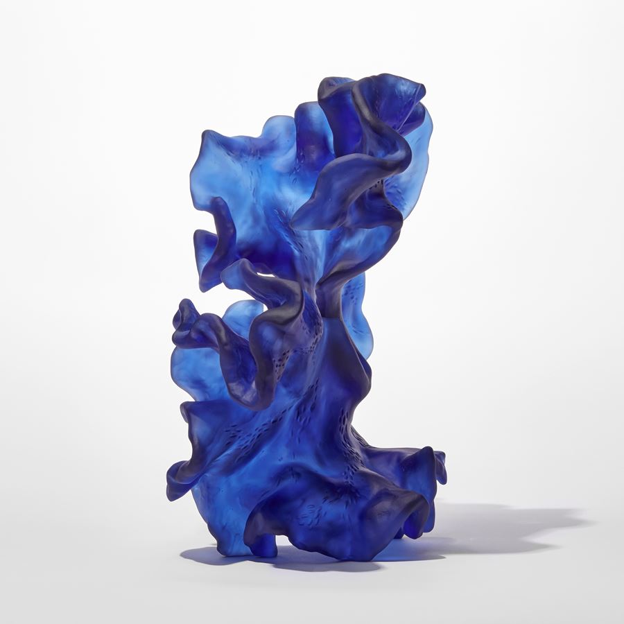 standing opaque blue frilled and undulating sculpture with the appearance of a piece of sea drift floating seaweed full of movement and made from cast glass