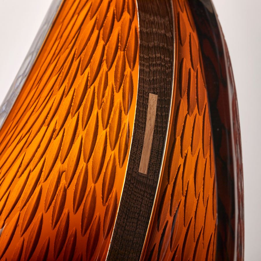stylised viking ship with curved oak hull and two sections of rich dark amber textured hand blown glass held aloft on a stainless steel and wood base 