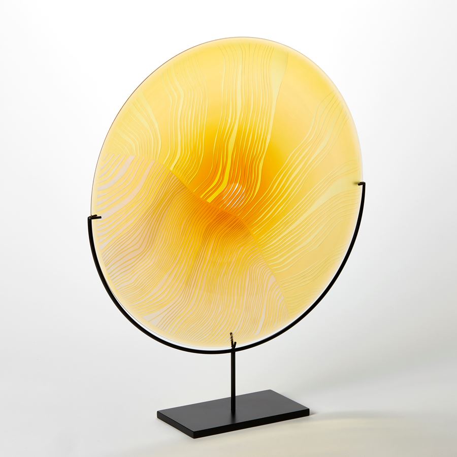 round yellow disc with surface cut abstract lines and patterns mounted on a matt black stand hand made from glass