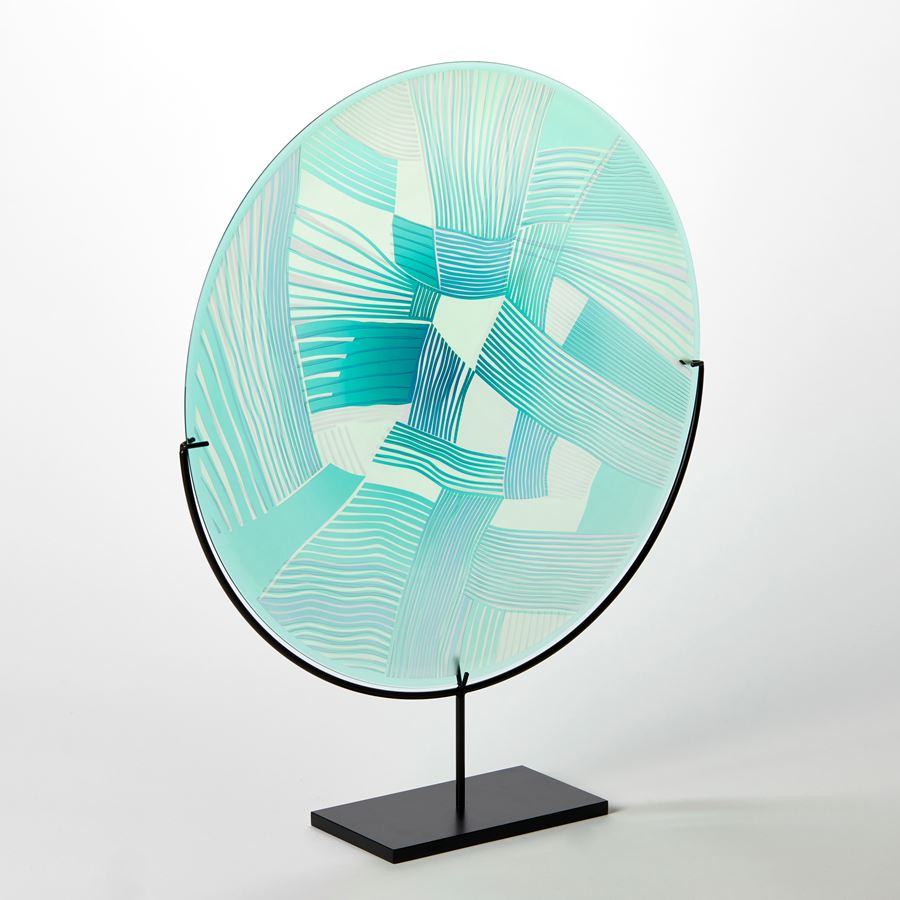 aqua and jade translucent round glass rondel with abstract patchwork landscape cutting on the surface handmade from glass and presented on a matt black steel stand