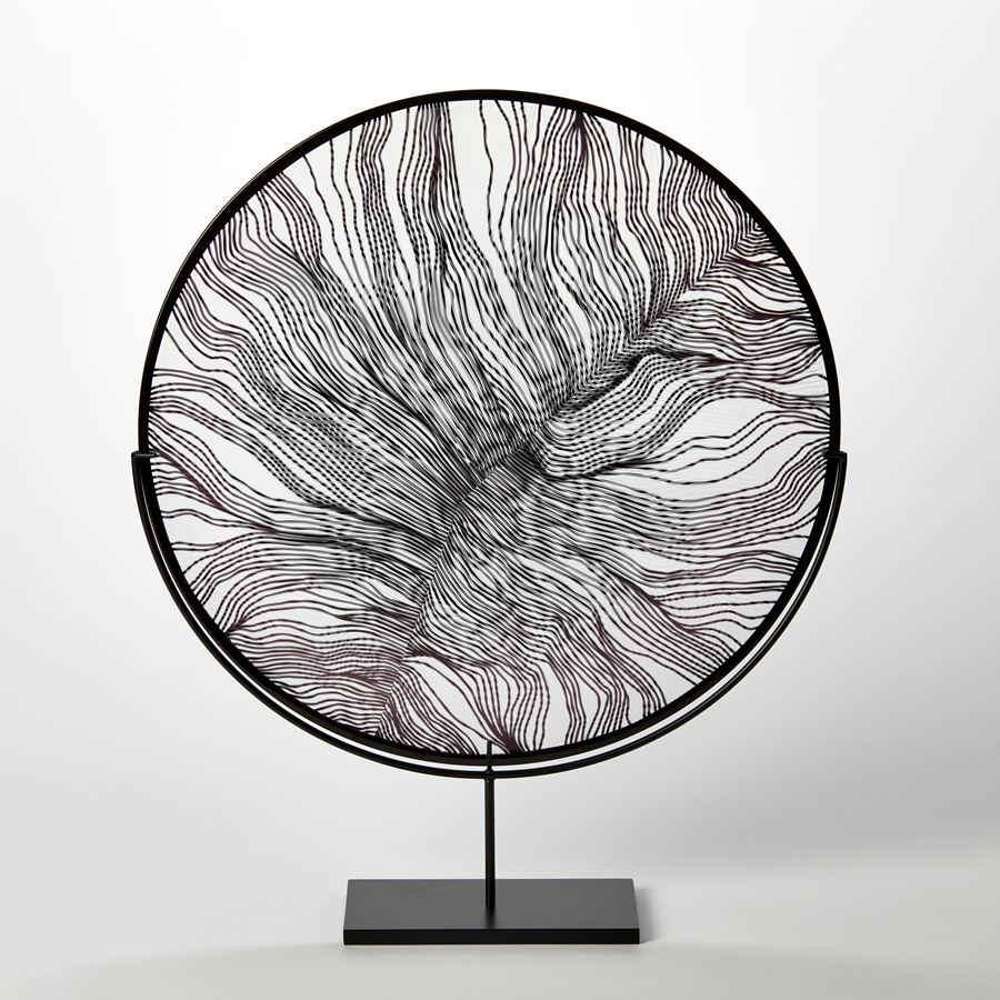 clear and black glass rondel with cut surface pattern resembling the details of a feather and a black rim hand made and presented on a matt black stand