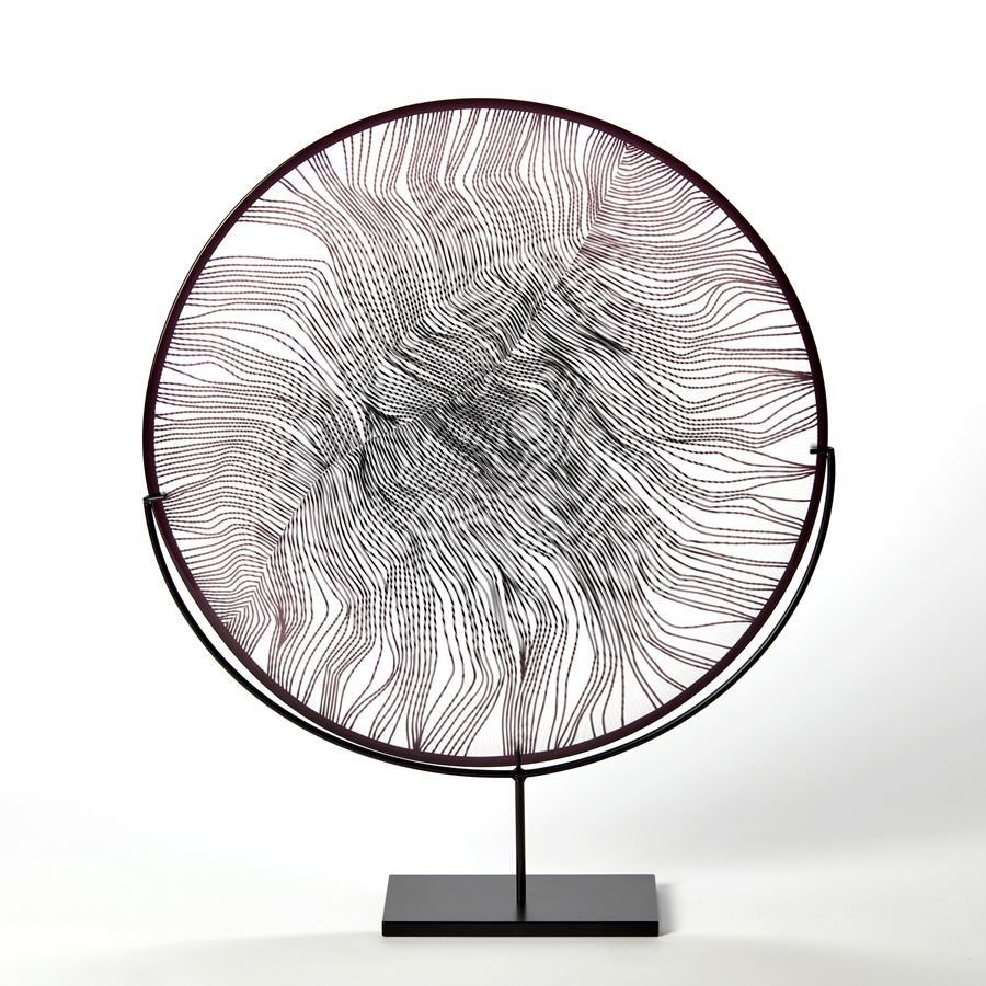 round clear and black glass plate with black rim and cut feather inspired surface pattern hand made and presented on a matt black steel stand 