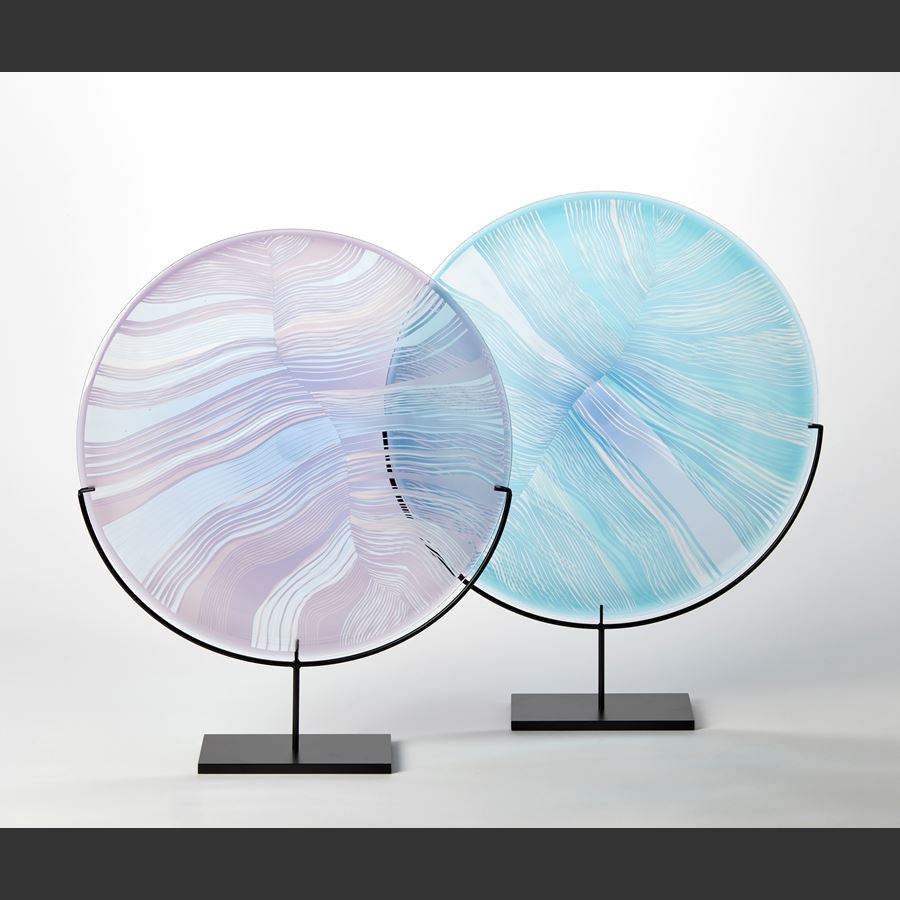 transparent aqua jade and clear glass disc mounted on a black matt stand with cut patterns on the front resembling the magnified details of a birds feather