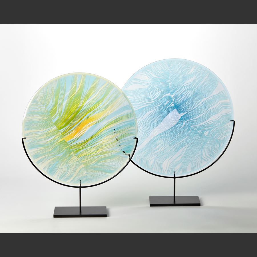 round glass rondel in soft light blue aqua and jade with front cut and etched linear patterns held aloft on a matt black stand