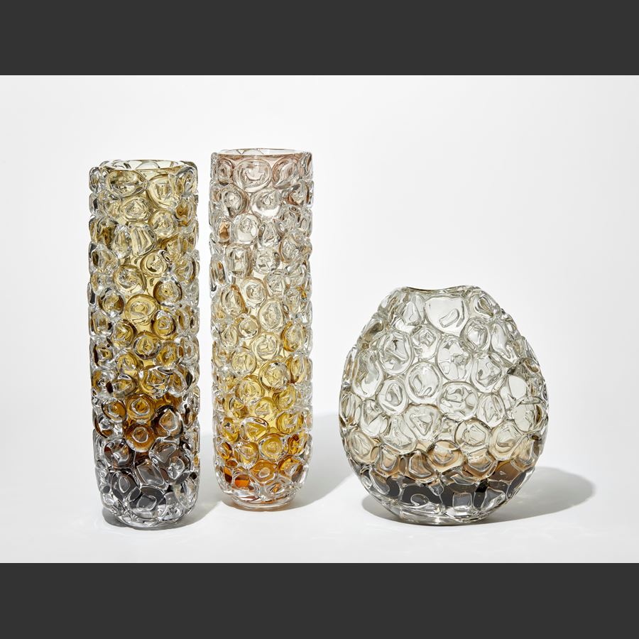 tall column shaped transparent vase with dark brown base fading to rich amber and olive at the top with the outside covered in oversized squished bubbles hand made from glass