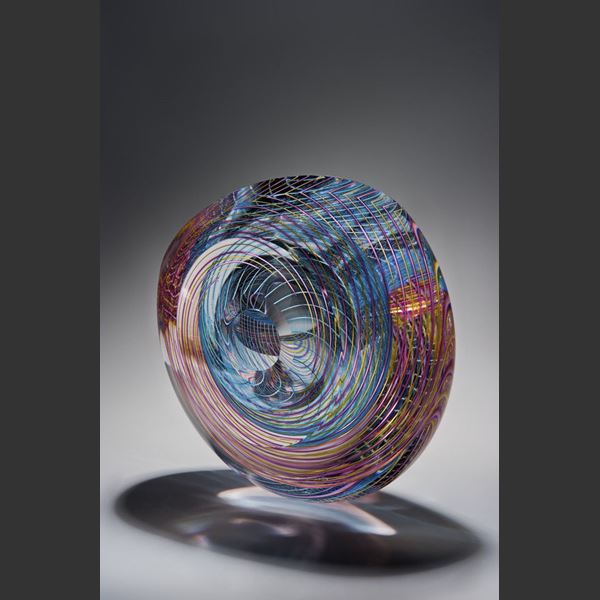 art glass sculpture in donut shape with geometric patterns in pink light blue and clear glass