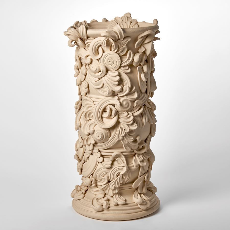 tall architectural vessel with the appearance of weathered sandstone covered in flourishes and swirls hand thrown and sculpted from white st thomas clay