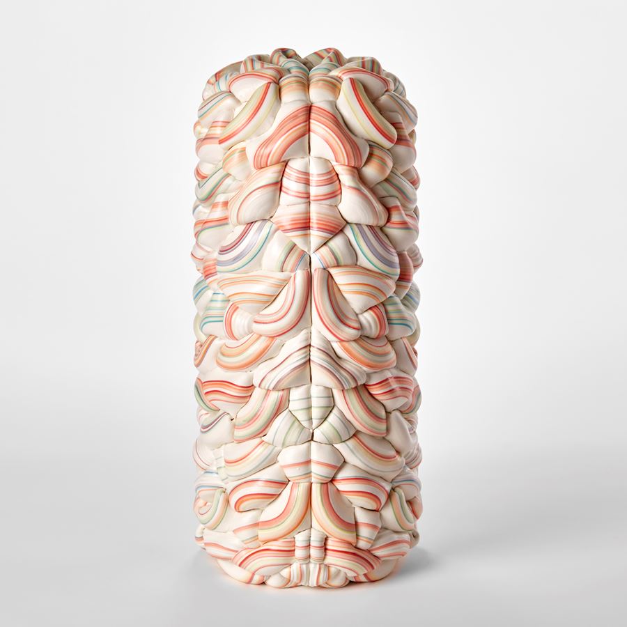 tall undulating and interwoven form in white with rings bands of bright colours in red pinks blues and turquoises with a central seam with each half mirroring each other hand made from parian porcelain