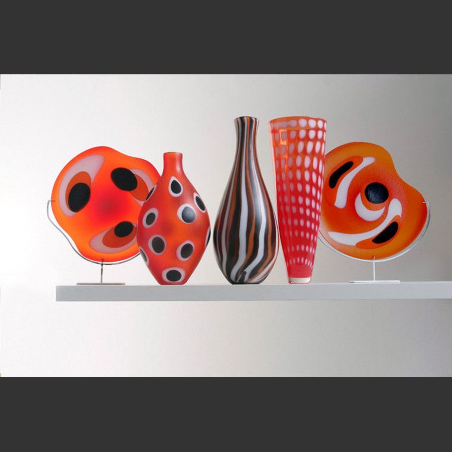 collection of five red art glass sculptures in different shapes with black and white patterns