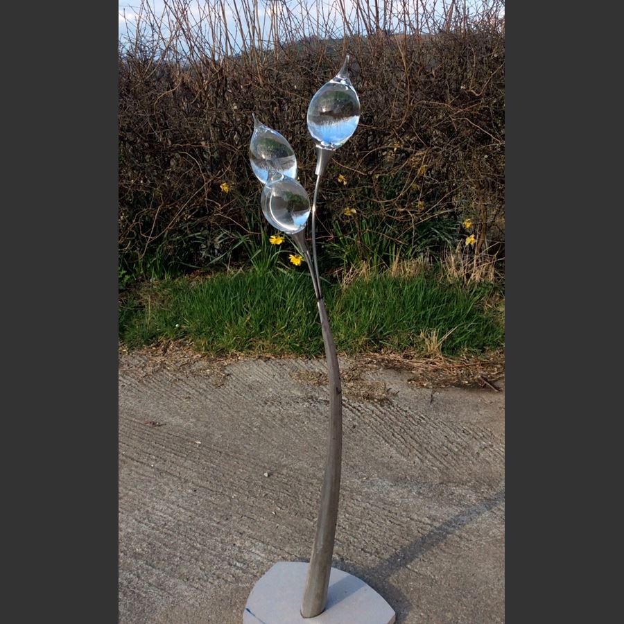 glass art in the shape of a lamp on steel base pictured outdoors