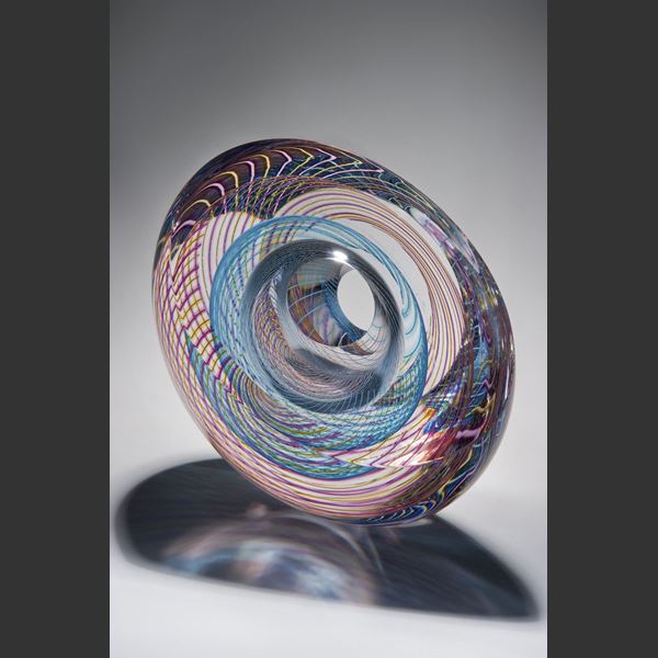 art glass sculpture in donut shape with geometric patterns in pink light blue and clear glass