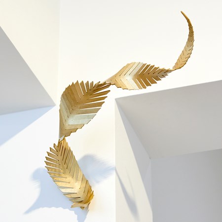 abstract angular curling feather with straight slits along the length and curling twisting form with a brushed finish and wall mounted as it just touching the surface