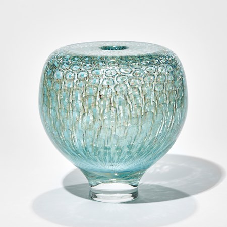rounded transparent vessel with tapered foot and a flat top with small opening hand made from thick handblown glass with a repeat pattern like tiny abstract jelly fish trapped under the surface in celadon olive teal and turquoise
